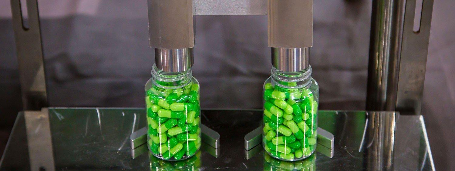 Two bottles being filled with green capsules by an automated counting and dispensing machine.
